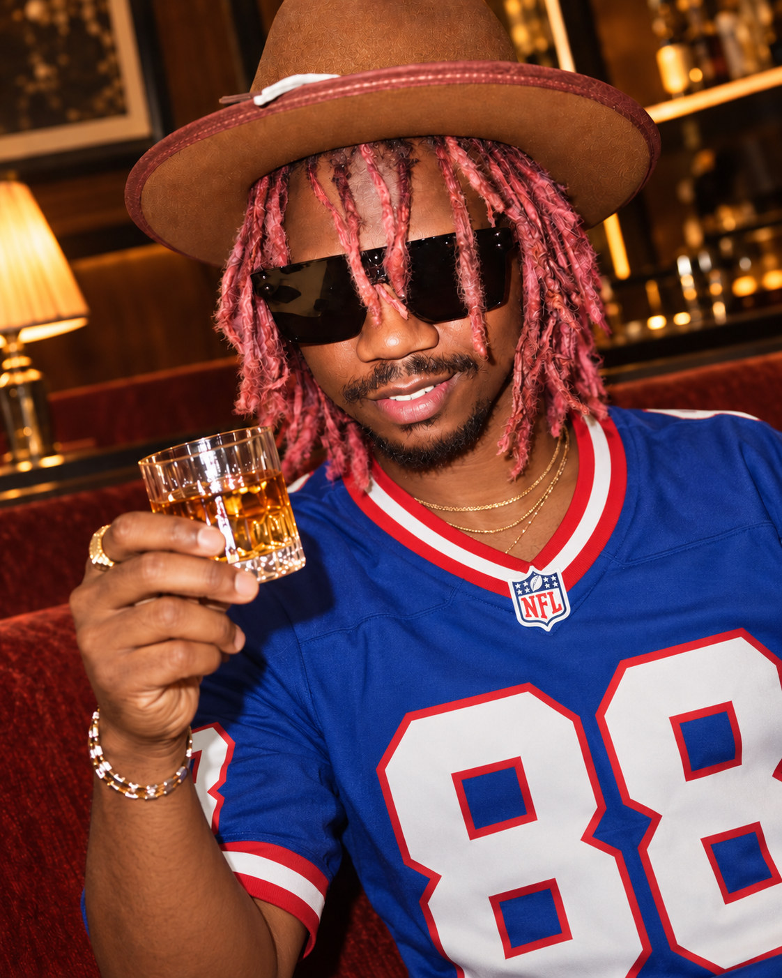 Prince Desire Magomo, Afri Kingdom, in a brown hat, sunglasses, and a blue 88 jersey, raising a glass.